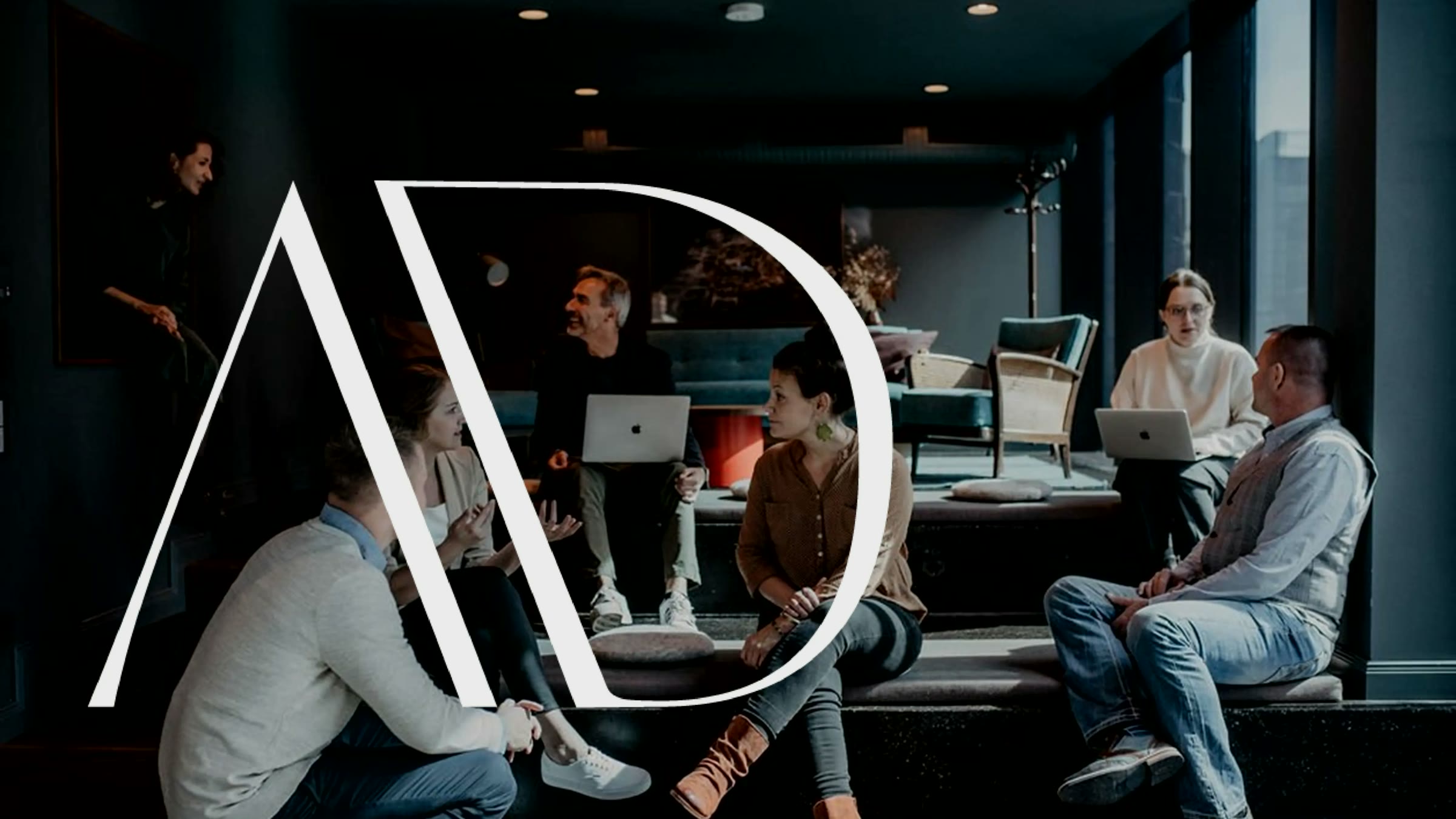AdSuits, Keyvisual mit dem AD-Monogramm über dem Team in der Agentur-Lounge