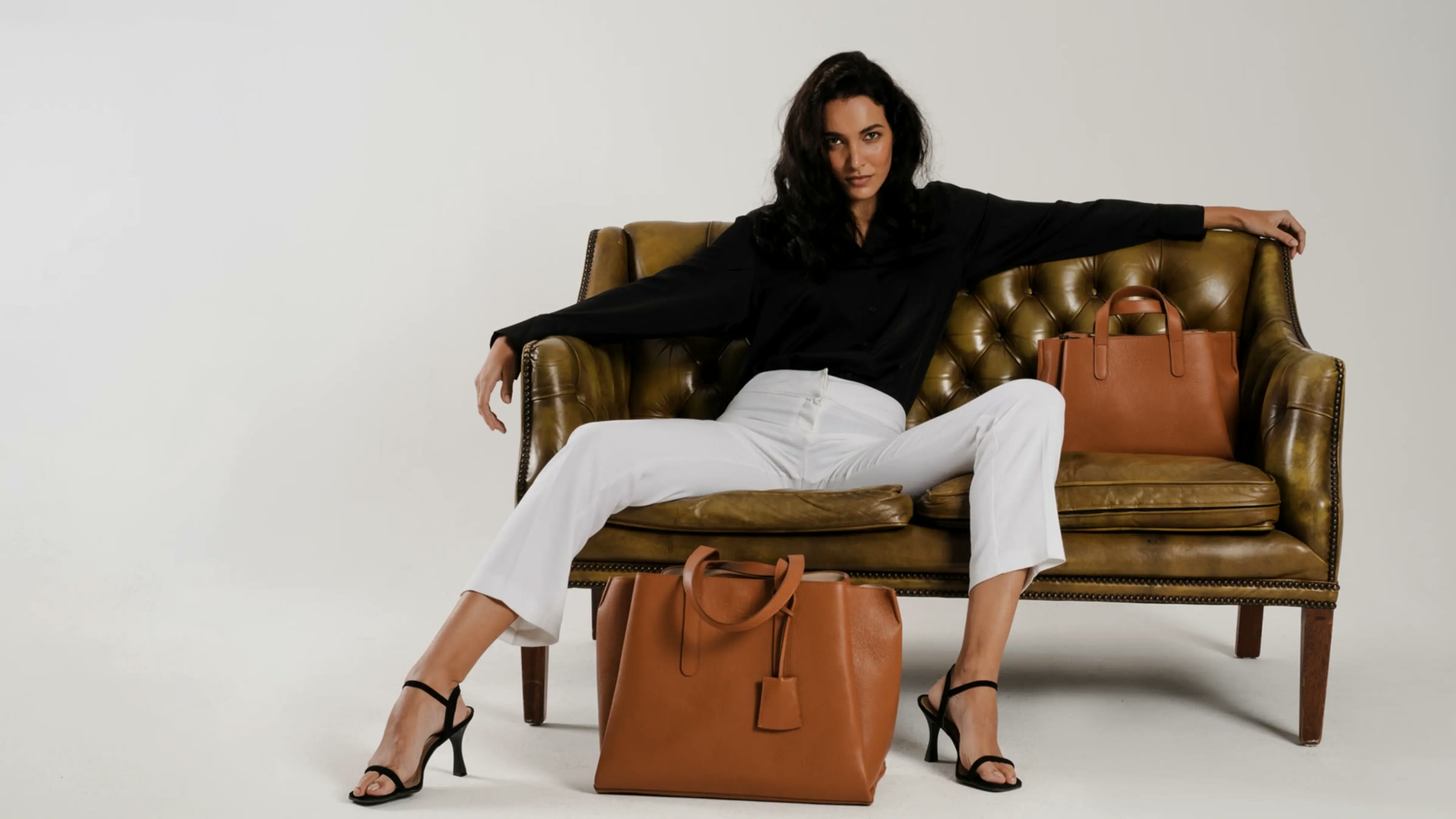 mine mina, Model mit cognacfarbener Ledertasche auf einem Chesterfield-Sofa
